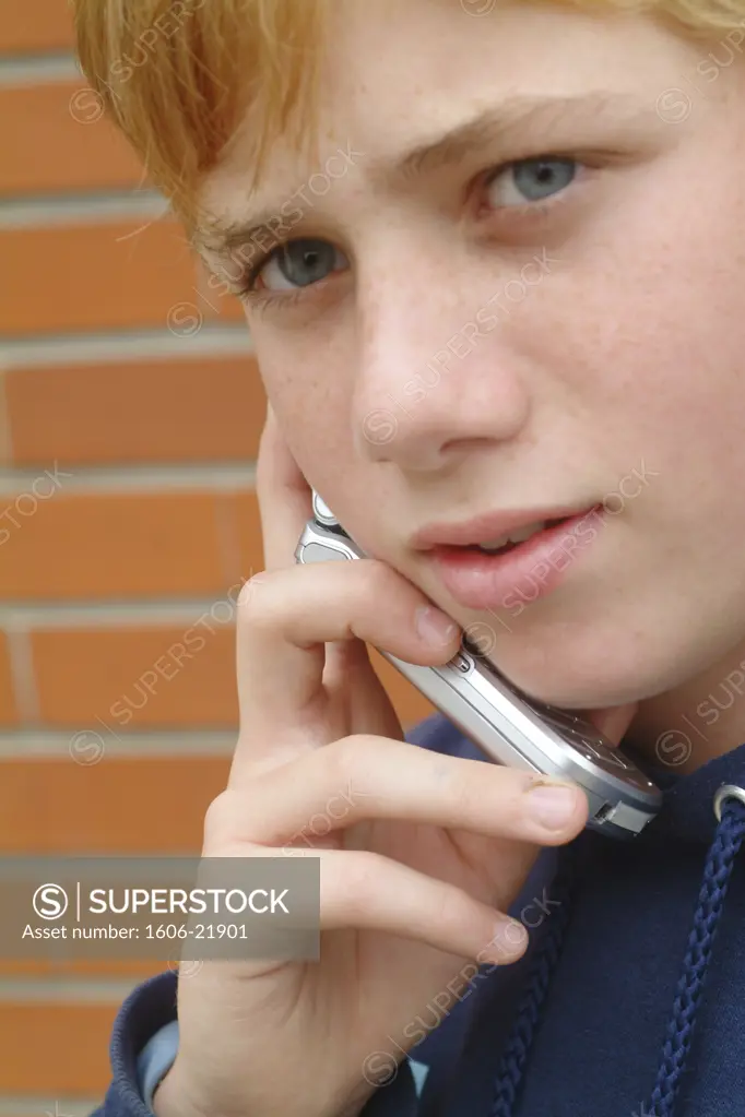 IN*Portrait adolescent roux posant, téléphonant avec mobile, fond mur en brique