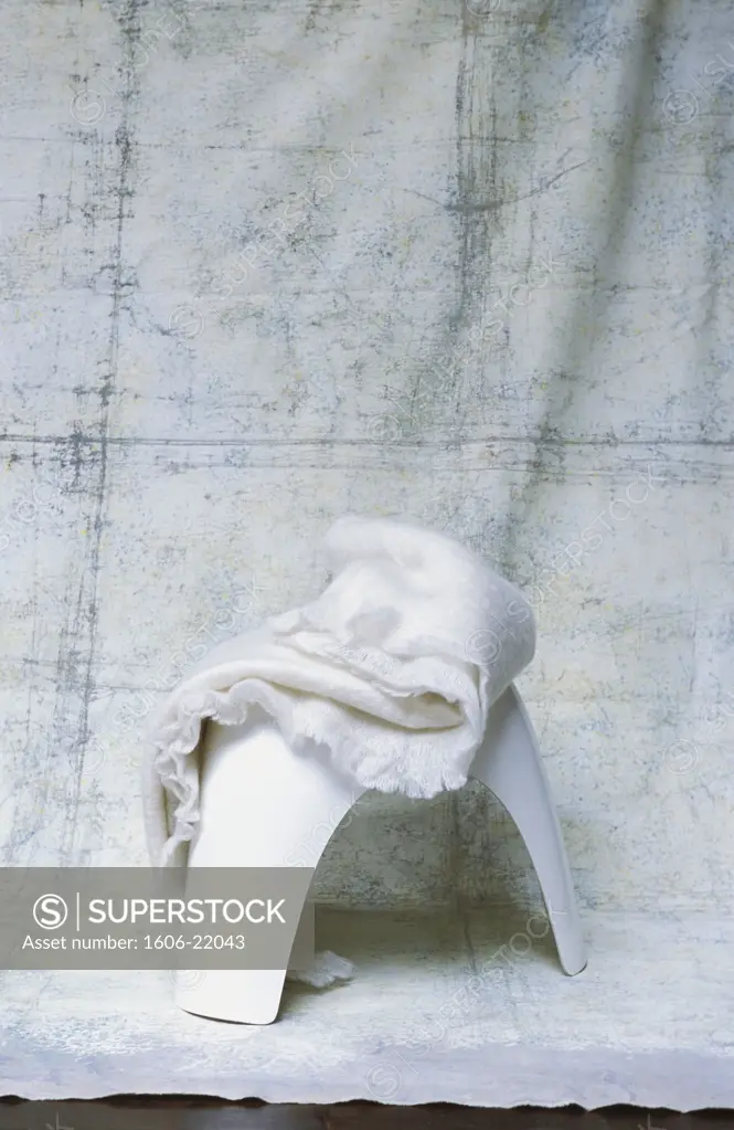 Gros plan sur couverture en laine mohair blanche sur tabouret blanc sur panneau en tissu peint en blanc
