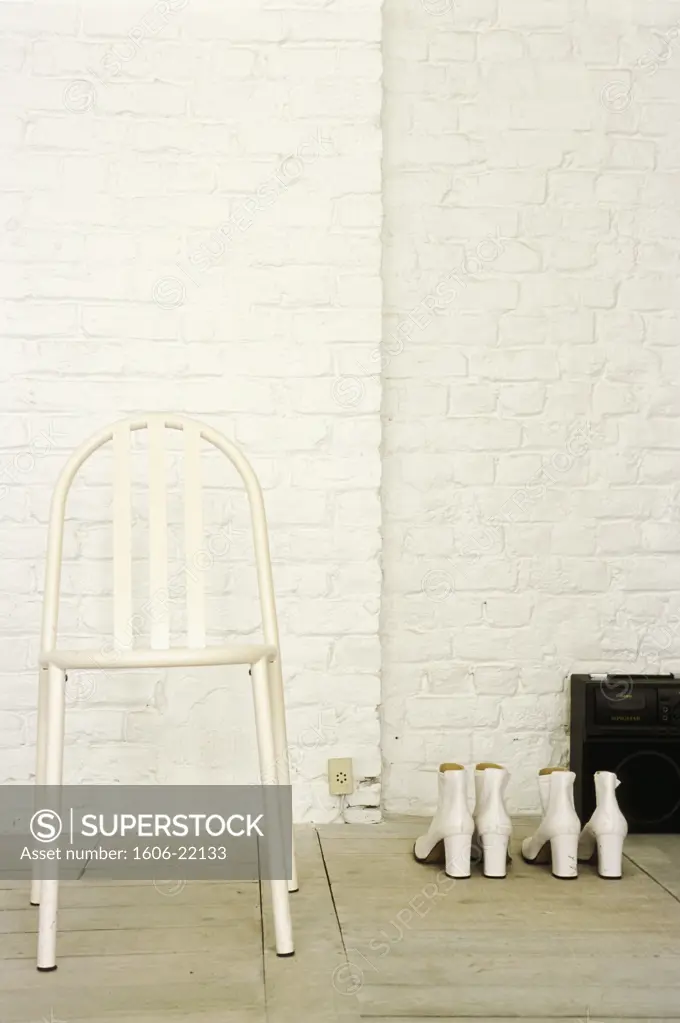 Chaise en métal laqué blanc sur parquet, 2 paires de bottines blanches en cuir sur sol, mur en briques peintes en blanc