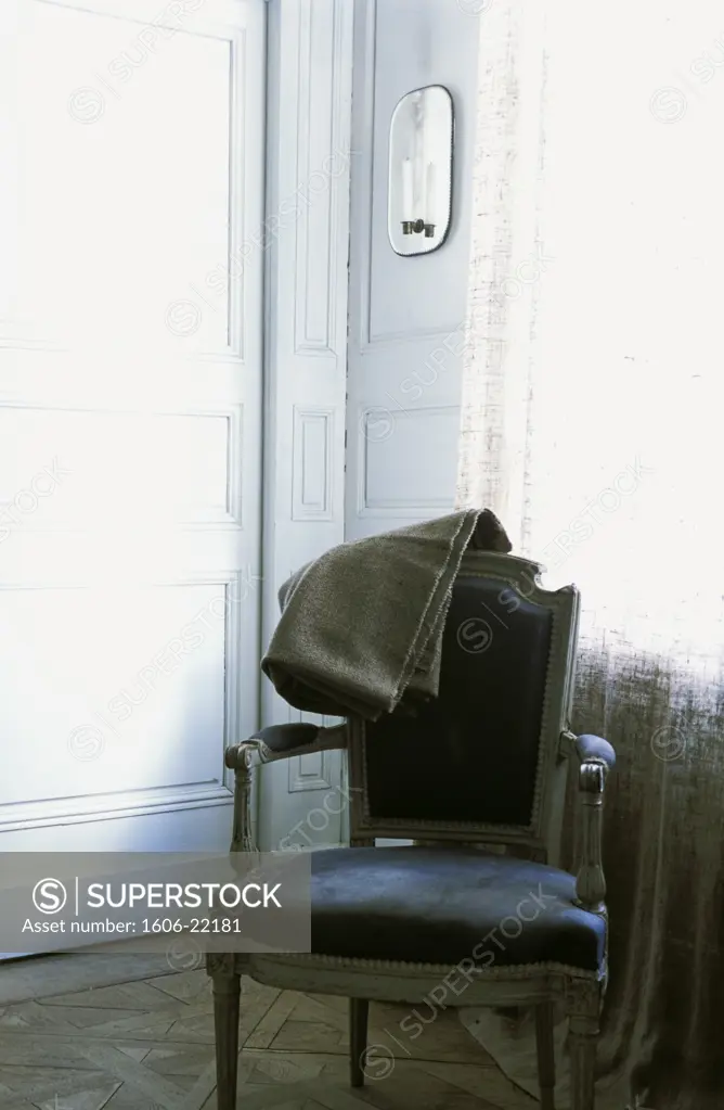 Intérieur séjour, plaid gris en flanelle sur fauteuil Louis XV  recouvert de velours violet, boiseries blanches, bougie sur applique avec miroir contre mur