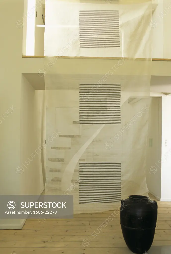 Intérieur séjour, vase noir sur parquet en bois clair, panneau de tissu blanc masquant escalier et étage