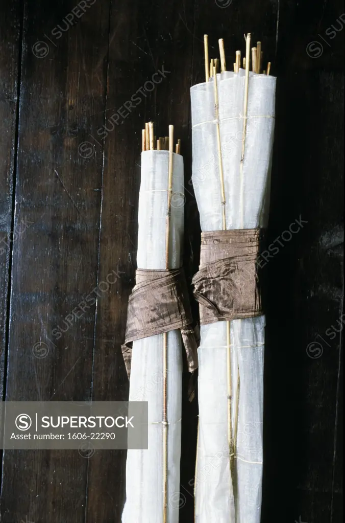 Gros plan sur 2 stores en soie blanche et baguettes de bambou, enroulés sur parquet en bois sombre