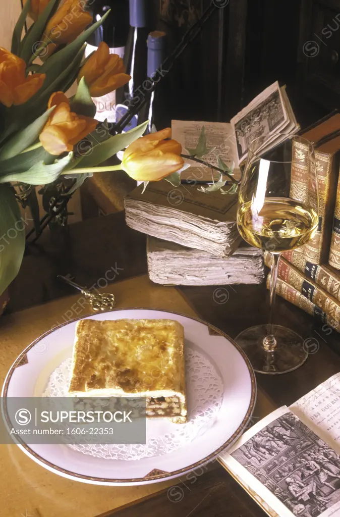 Composition part de gateau feuilleté au chocolat sur assiette blanche, livres anciens et bouquet de tulipes sur table, verre de vin blanc