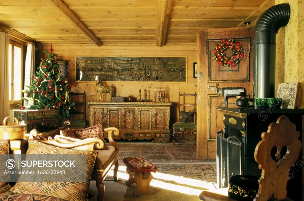 Intérieur chalet ancien, cheminée, meuble en bois peint, au fond, tapis, canapé, sapin de Noel près fenêtre