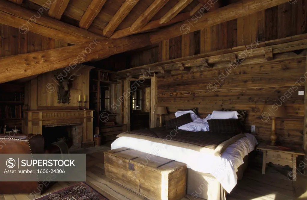 Val d'Isère, intérieur chambre, murs en lambris, coffre ancien au pied du lit, cheminée en bois, fauteuil en cuir