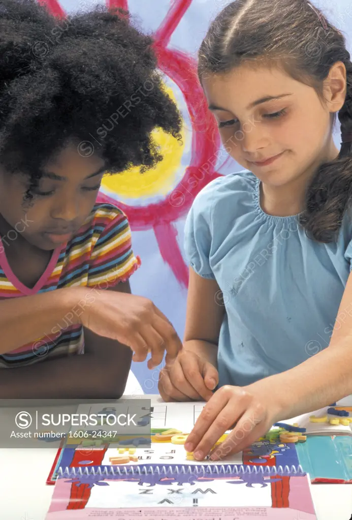 Deux petites filles, l'une blanche, l'autre noire,jouent avec les lettres del'alphabet d'un jeu éducatif