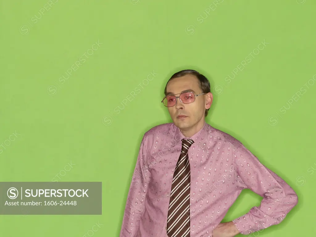 Man, slicked hair, smoked glasses, polka-dot shirt and striped tie, green background, posing, arms akimbo, for the camera