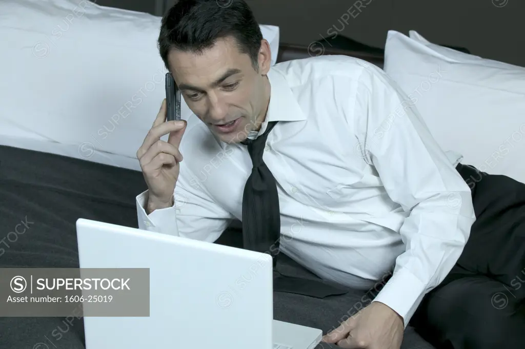 IN*Valery téléphonant allongé sur lit, regardant ordinateur portable, chemise blanche, cravate noire