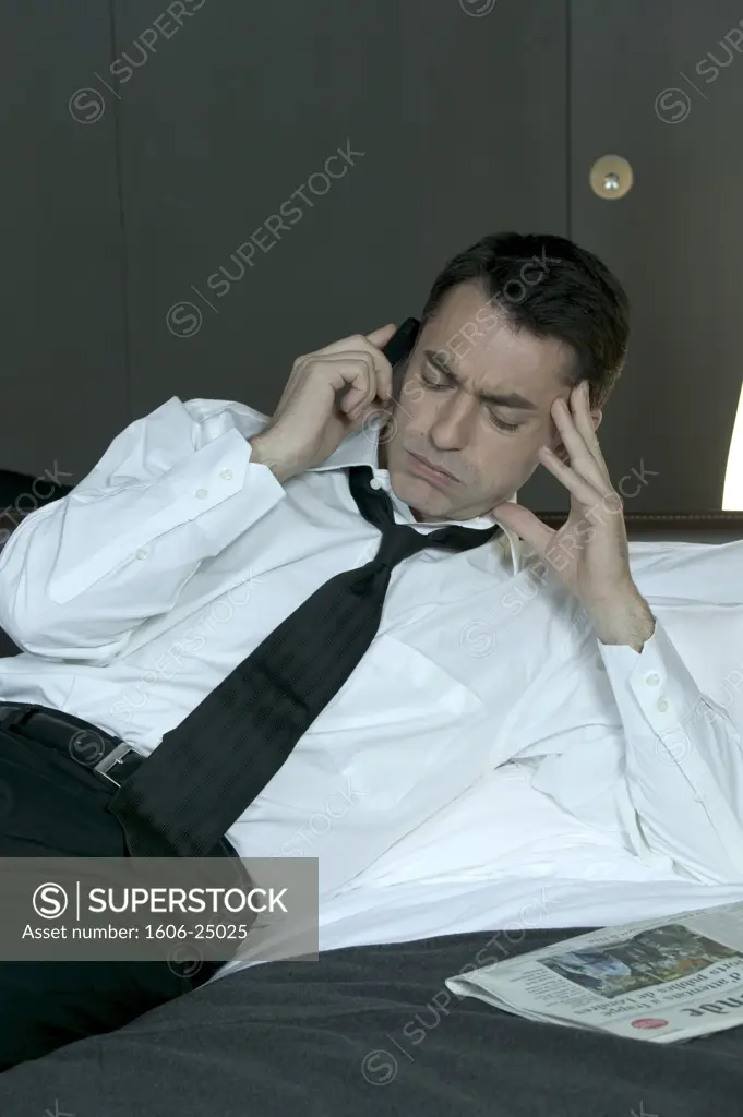 IN*Valery téléphonant allongé sur lit, air contrarié, chemise blanche, cravate noire