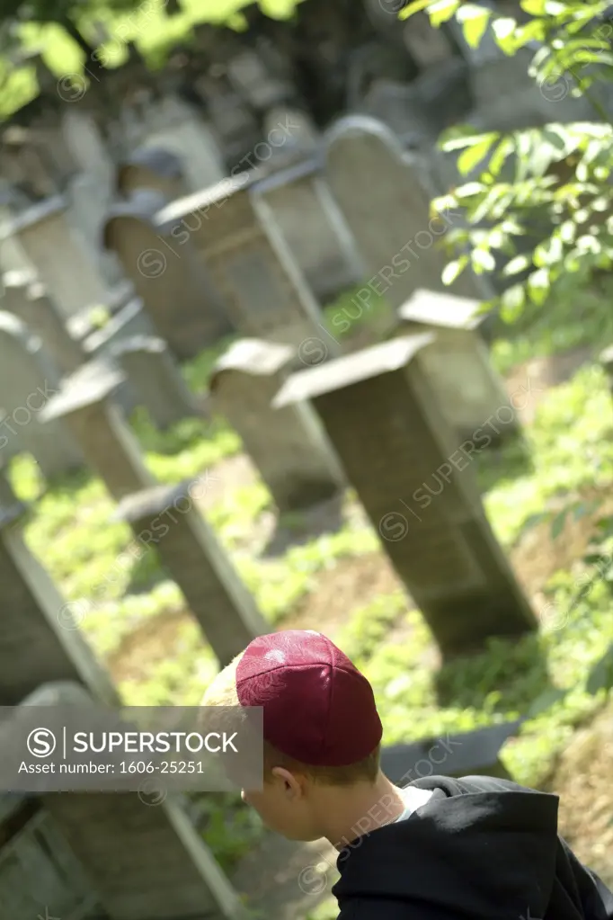 IN*Pologne, Cracovie, cimetière juif, petit garçon avec kippa rouge marchant parmi pierres tombales, verdure