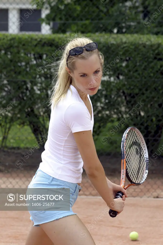 IN*Sophie jouant au tennis, short bleu et tee-shirt blanc, lunettes de soleil sur les cheveux