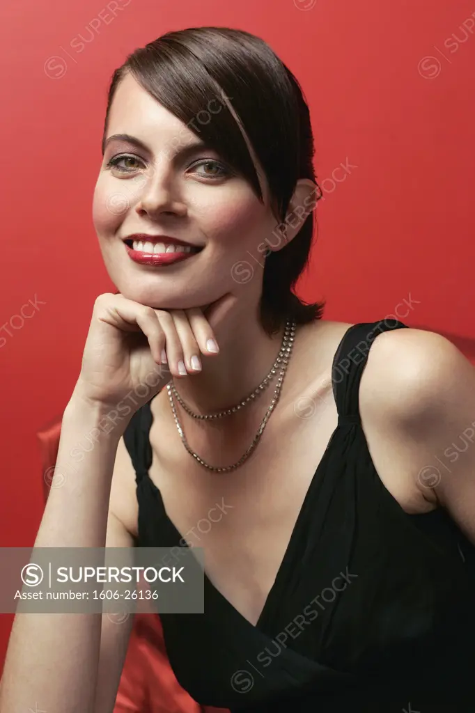 IN*Portrait Ema posant, souriante, maquillée, en intérieur, débardeur noir, fond rouge