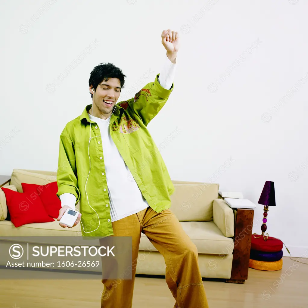Boy smiling, eyes closed, listening to music with Ipod, arm up, beige sofa in background