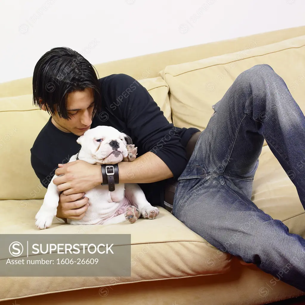 Boy sitting on beige sofa, holding bulldog against him