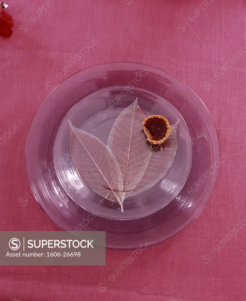 IN*Gros plan sur petite tartelette sur 2 assiettes en verre mauve, feuilles en tissu transparent, nappe en lin rose