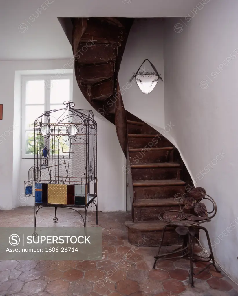IN*Intérieur maison ancienne, escalier en bois en colimaçon, grande cage à oiseaux sur sol en tomettes, murs blancs