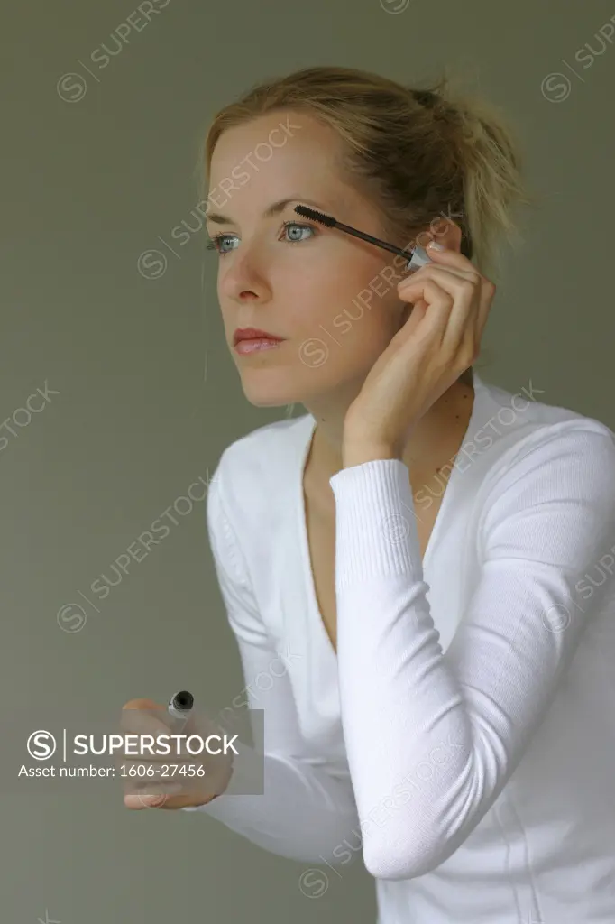 Portrait girl, white pullover, applying mascara, green background