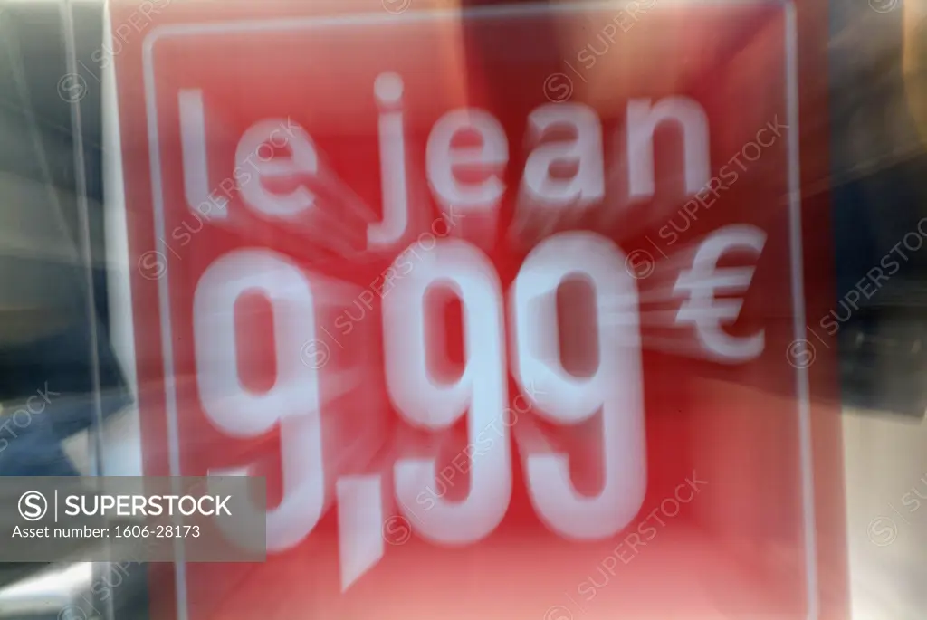 Close up on red sticker with white inscriptions « le jean 9,99  » (jeans 9.99) on shop window