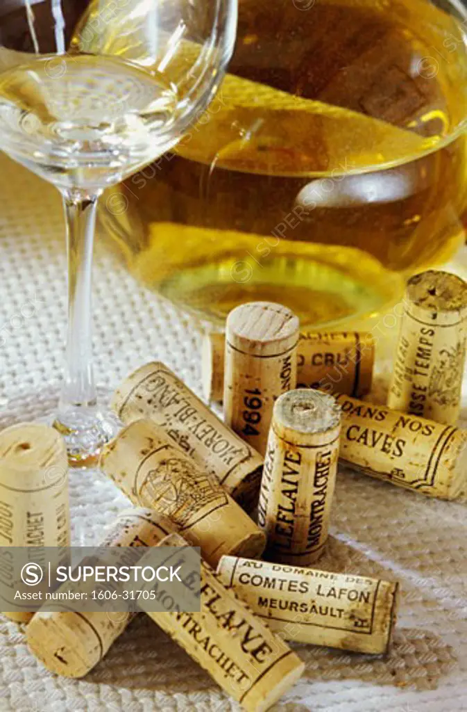 France, Burgundy, Côte-d'Or, Puligny, close-up on carafe and glass of white wine, corks from. various wine cellars