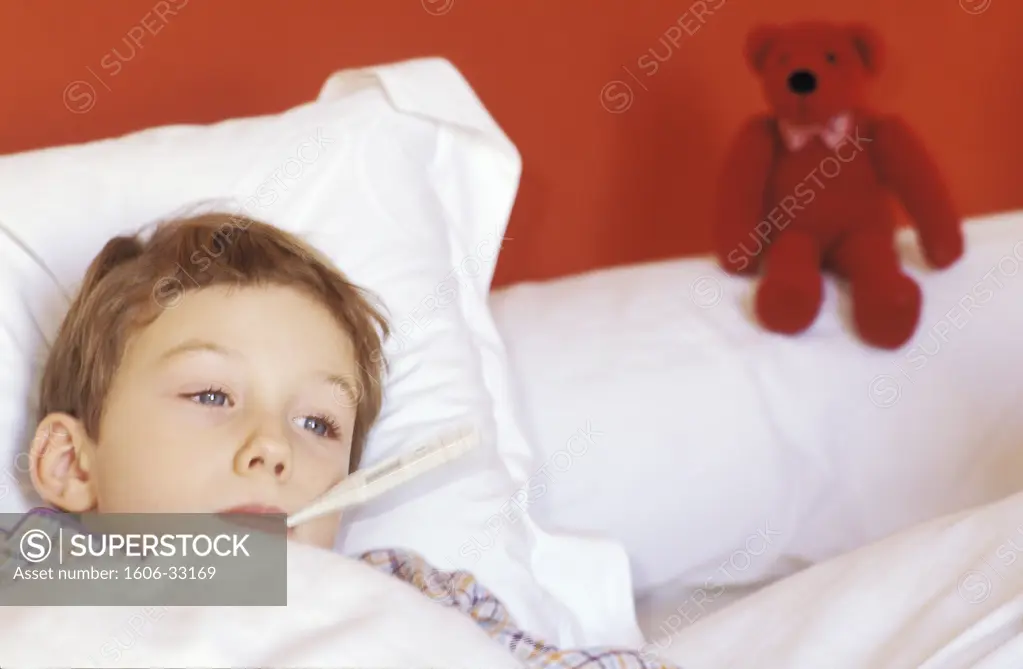 Boy lying in bed, thermometer in his mouth, red teddy bear on bolster