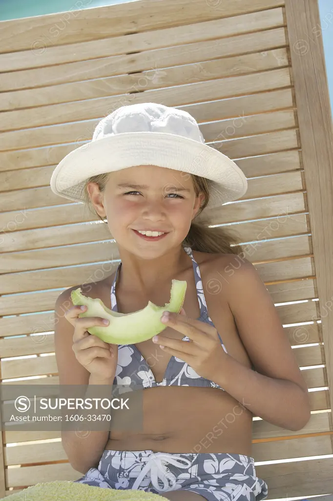 Portrait girl smiling, holding slice of watermelon, sitting on wooden deckchair