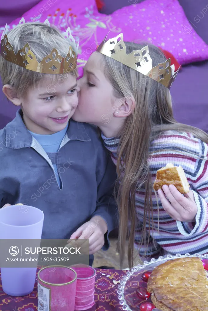 Little girl with slice of "galette des Rois" (cake eaten in France on Twelfth Night), kissing little boy