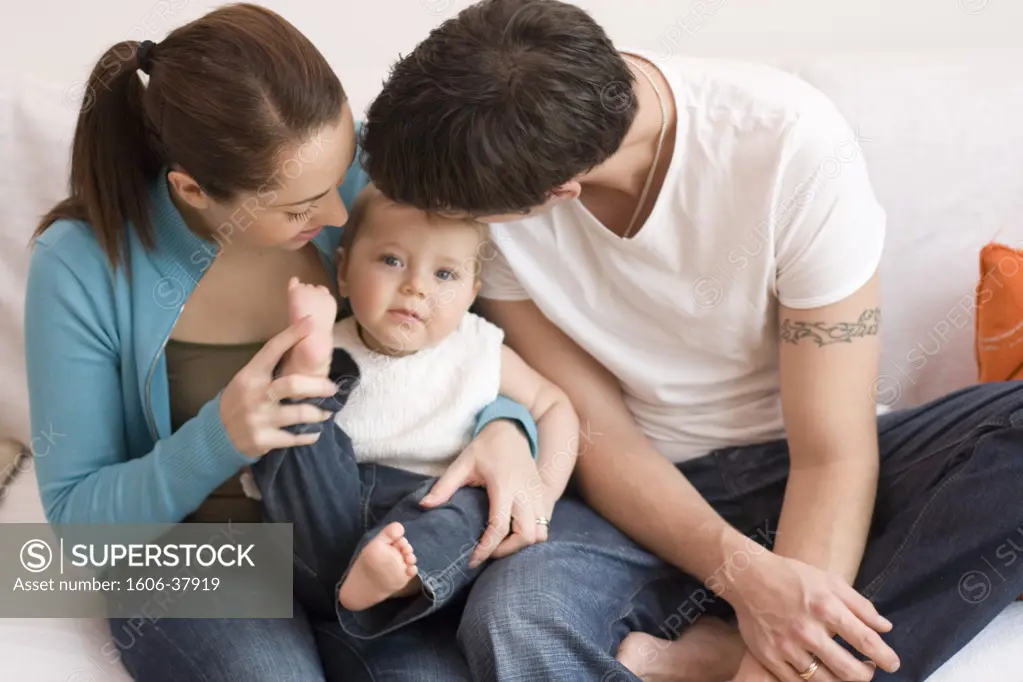 Parents sitting on sofa, looking at their baby boy, seated between them both