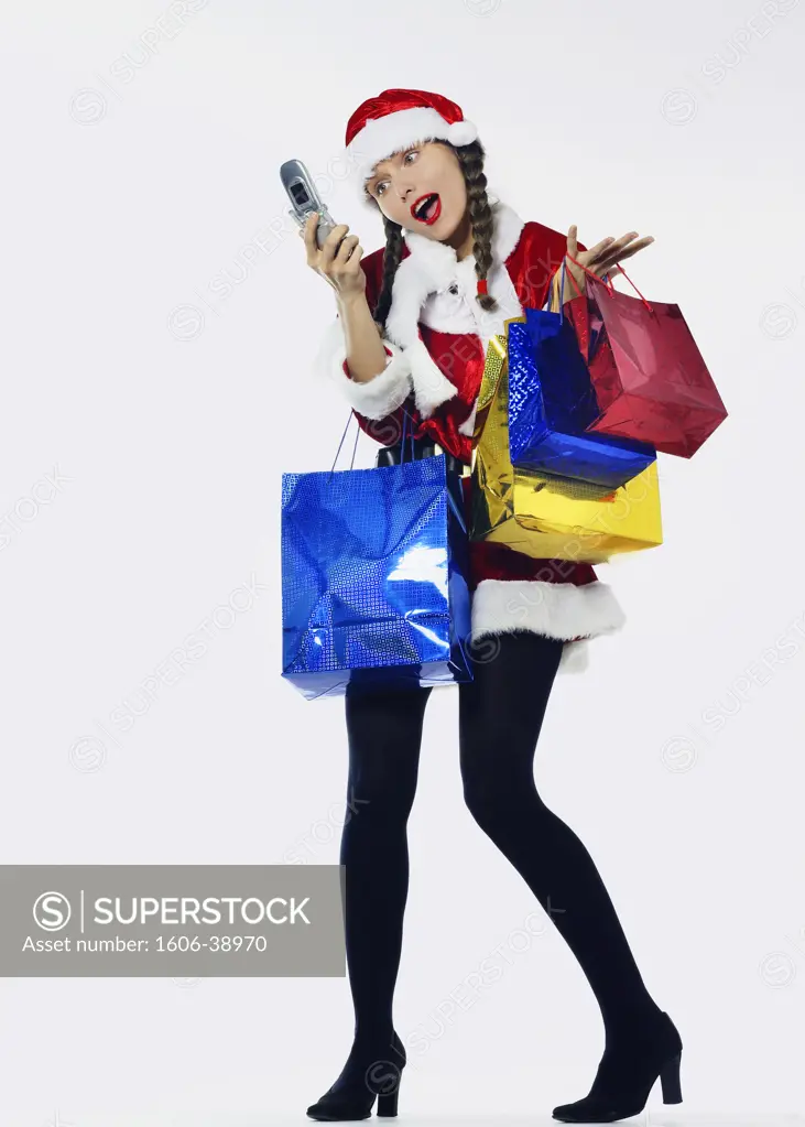 Woman dressed up in Santa Klaus, 4 shopping bags, looking et screen of her cell phone