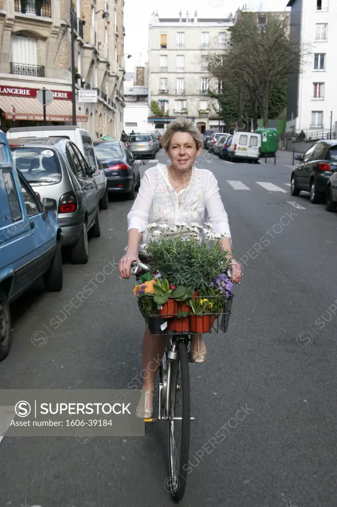 IN*Paris, 11ème, femme blonde à vélo dans rue, pots de fleurs sur porte bagages sur guidon