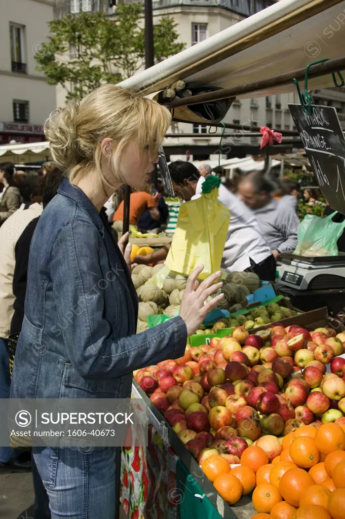 Woman in marketplace in front of an array of fruits