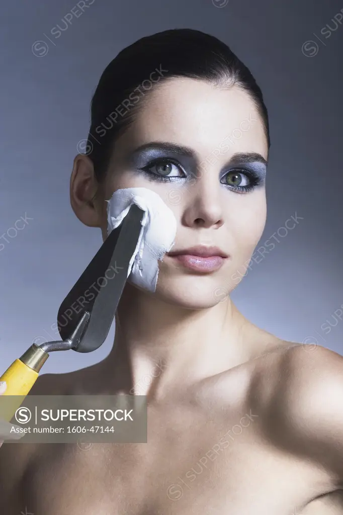 Portrait of a woman applying plaster on her cheek with a trowel