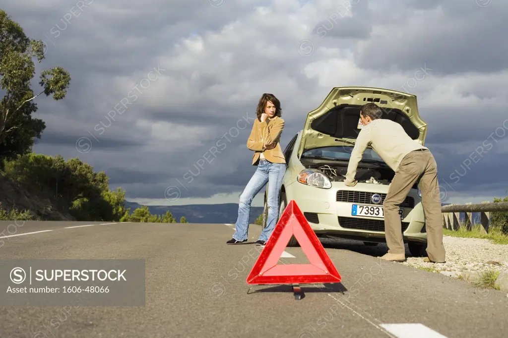 Man looking under the car hood, woman waiting