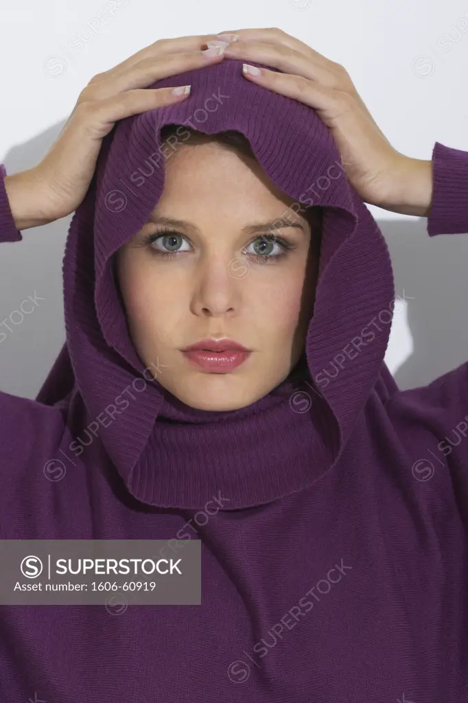 Portrait of woman wearing a violet pull-over with cowl collar, hands on her head