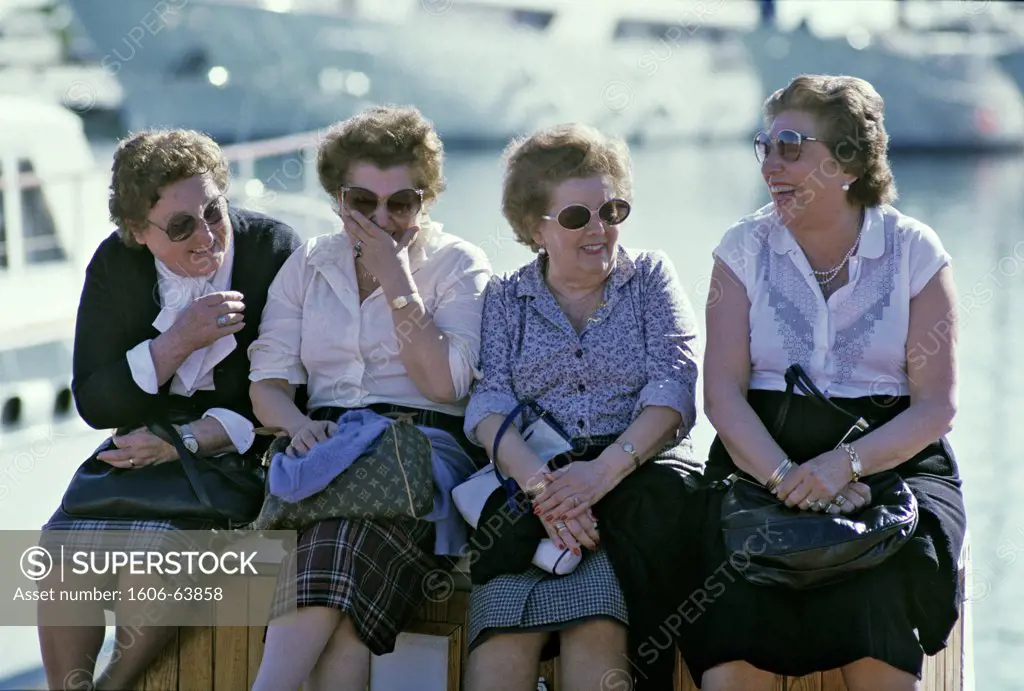 Four old women sitting on a harbour, laughing