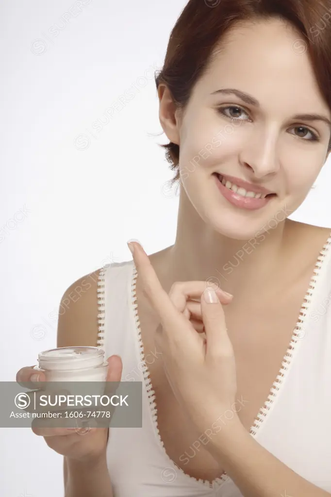 Portrait of a young brunette woman smiling with forefinger smeared with cream