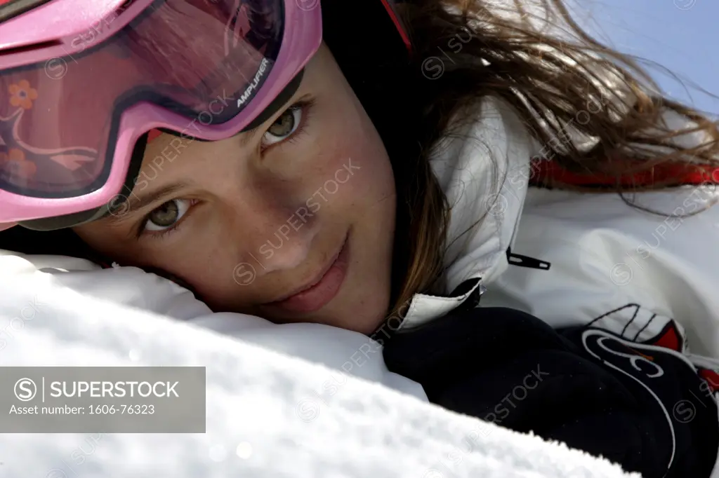Portrait of young girl lying in snow, with ski goggles