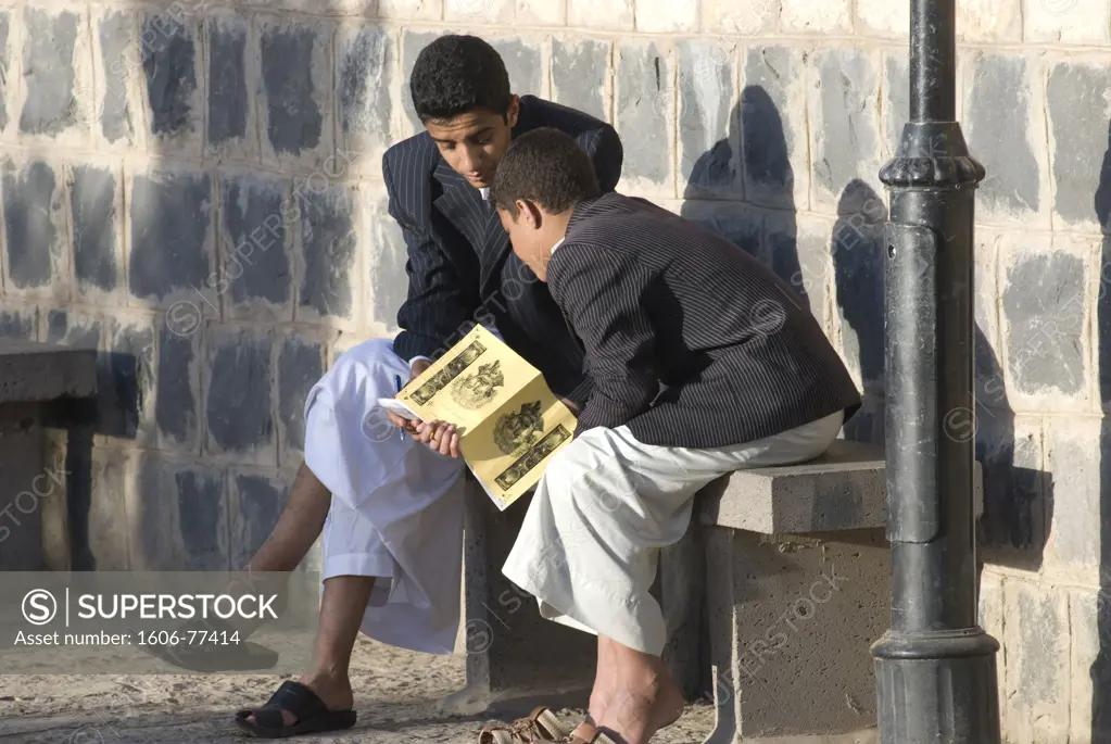 Yemen, Sanaa, two little boys looking at a book, in the street