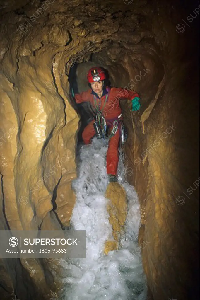 Speleology, caving, caver in a small gallery with an underground river, Grotte de la Cabane, Aveyron (France)