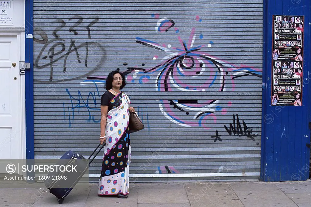 England,London,Brick Lane,Asian Woman with Suitcase in front of Graffiti Covered Shop Front Shutters