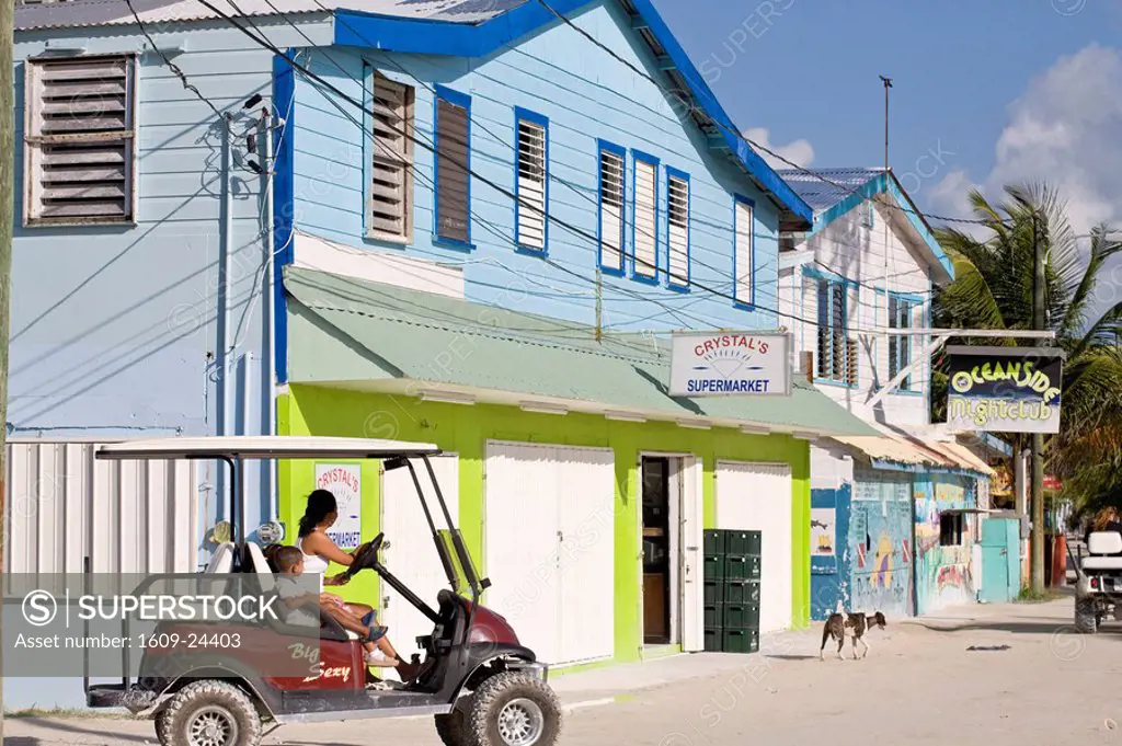 Belize, Caye Caulker, Woman driving golf cart past supermarket