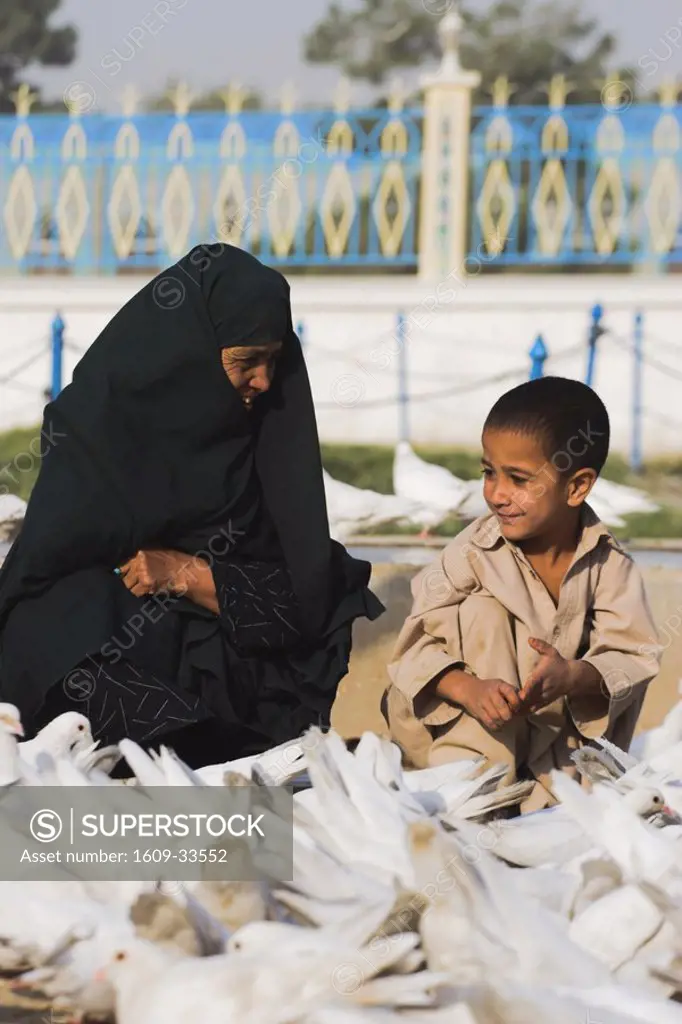 Afghanistan, Mazar-I-Sharif, Lady wearing burqa & son feeding white pigeons at Shrine of Hazrat Ali