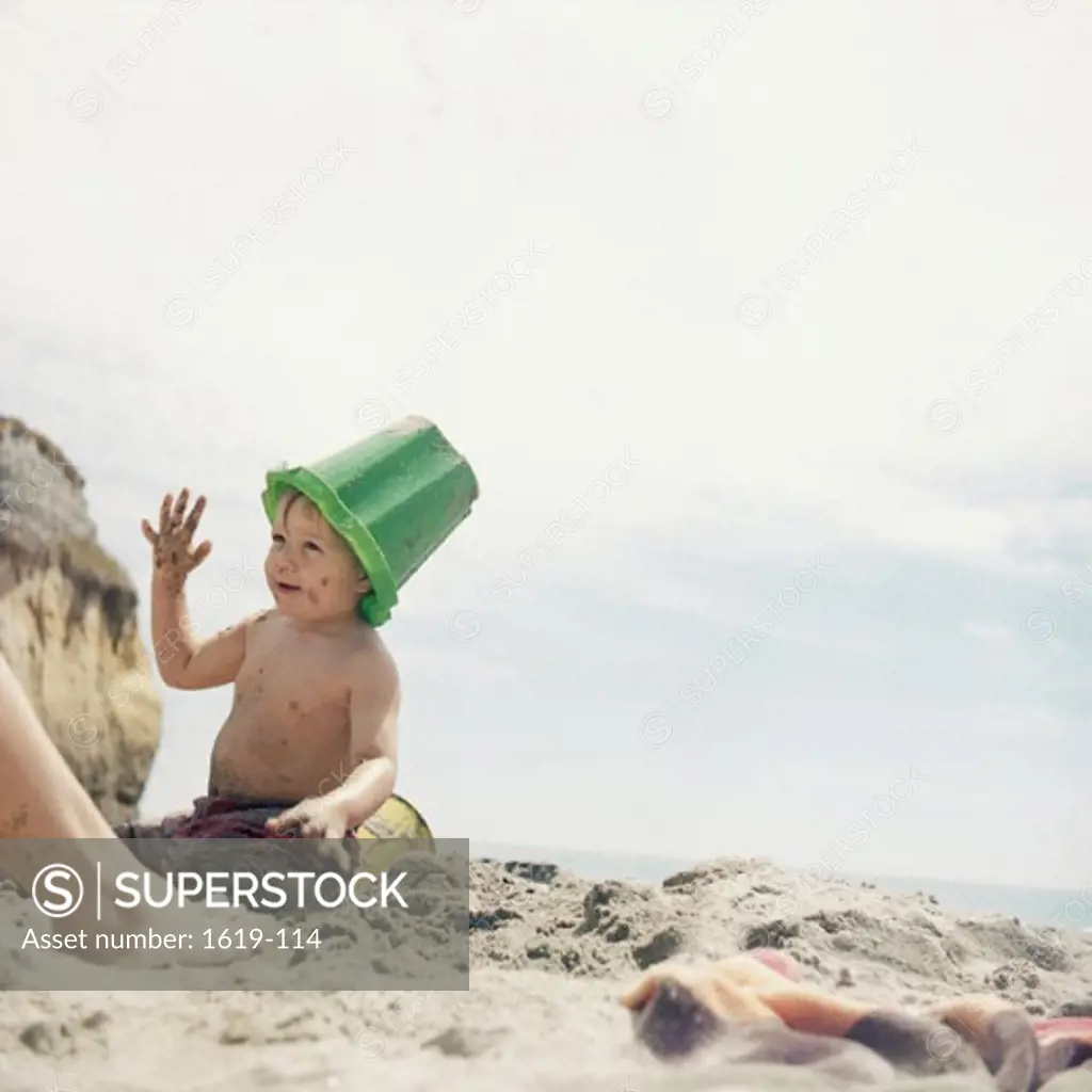 Boy with a bucket on his head playing on the beach