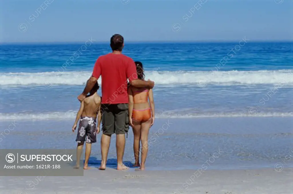 Rear view of a father standing with his son and daughter on the beach