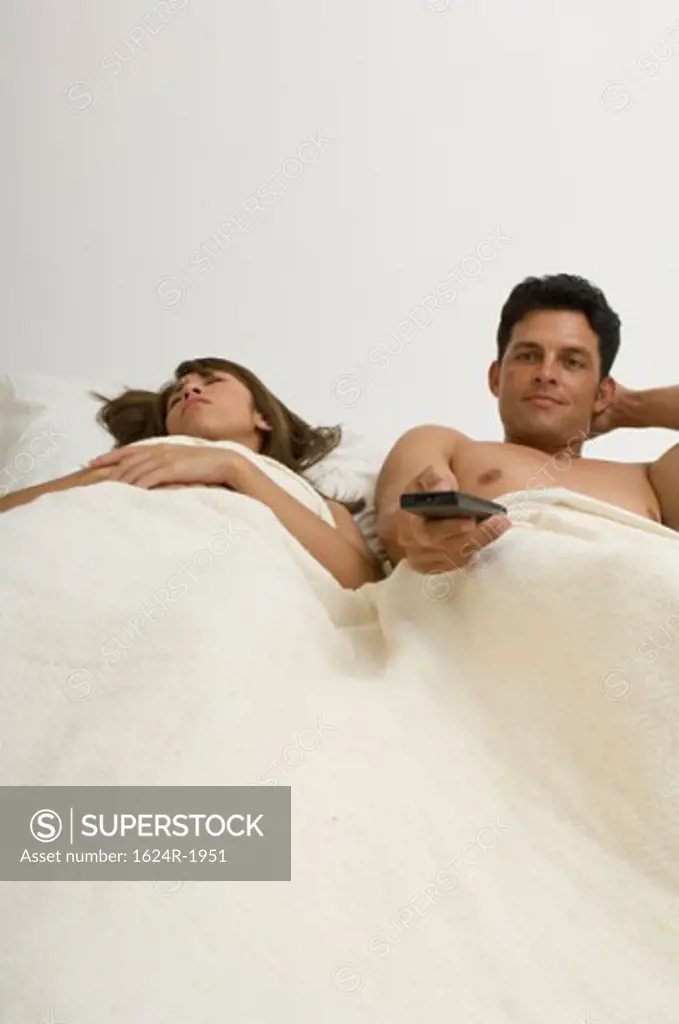 Portrait of a man watching TV in bed while his wife sleeps.