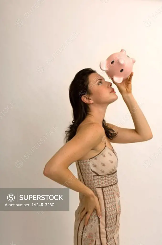 Portrait of a woman checking her piggy bank for money.