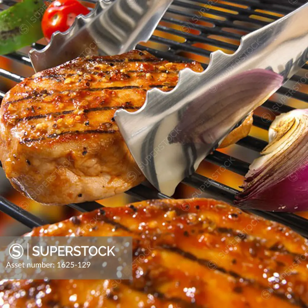 Close-up of grilled pork chops with tongs on a barbecue grill