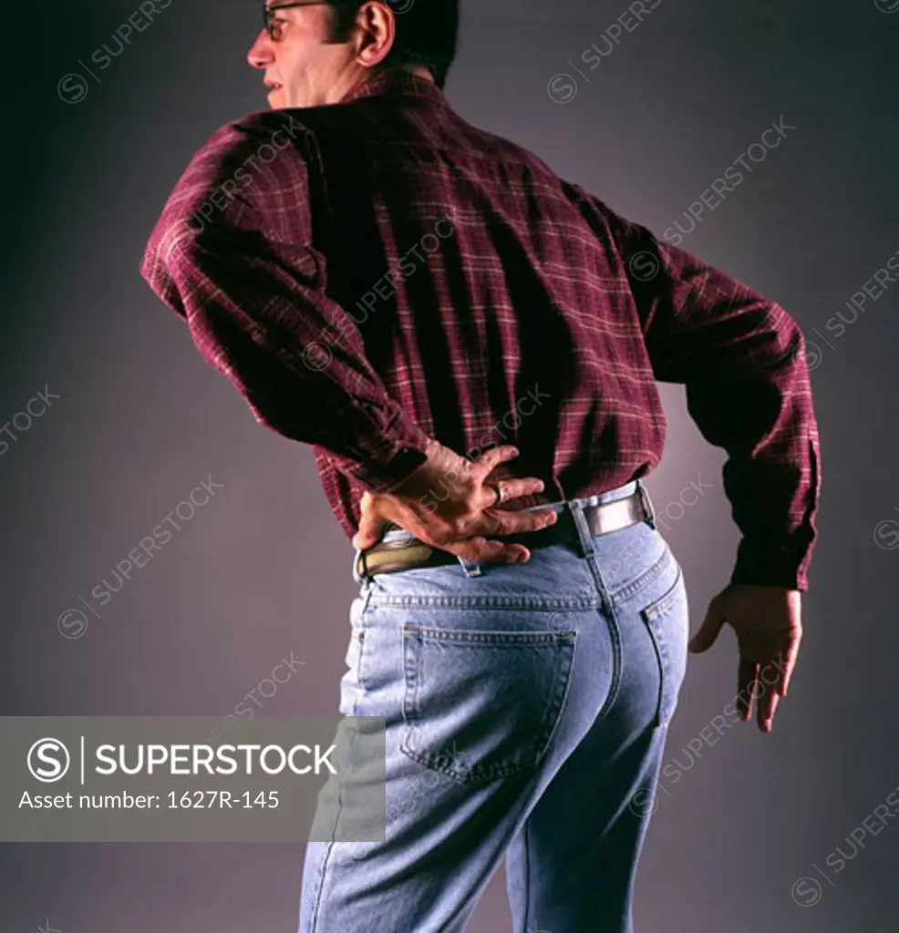 Rear view of a mid adult man bending forward touching his back in pain