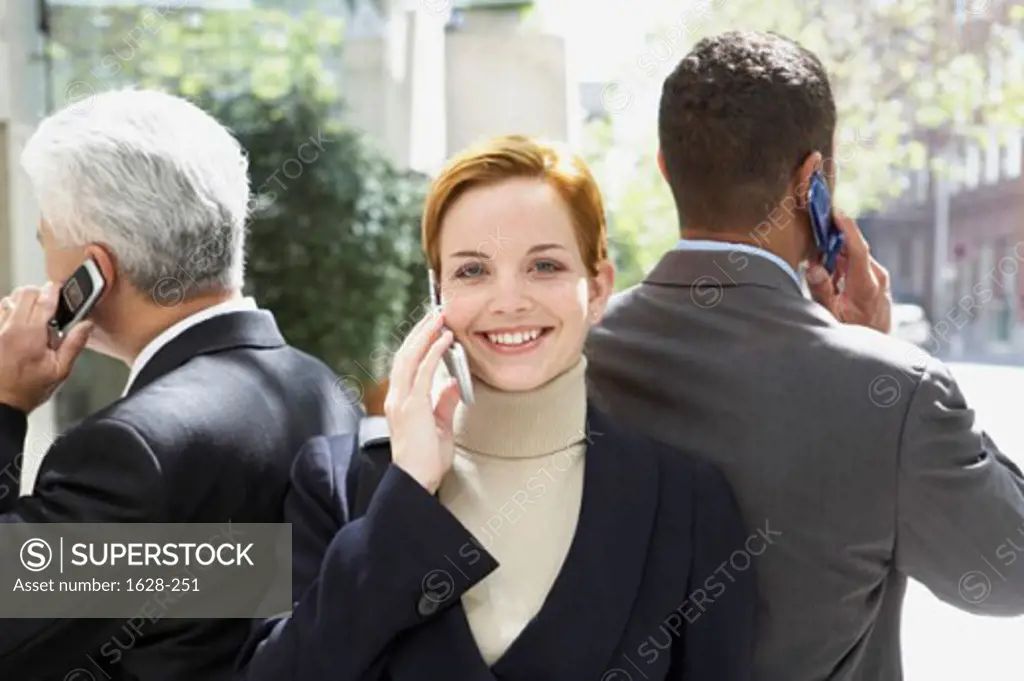 Portrait of a businesswoman with two businessmen talking on mobile phones