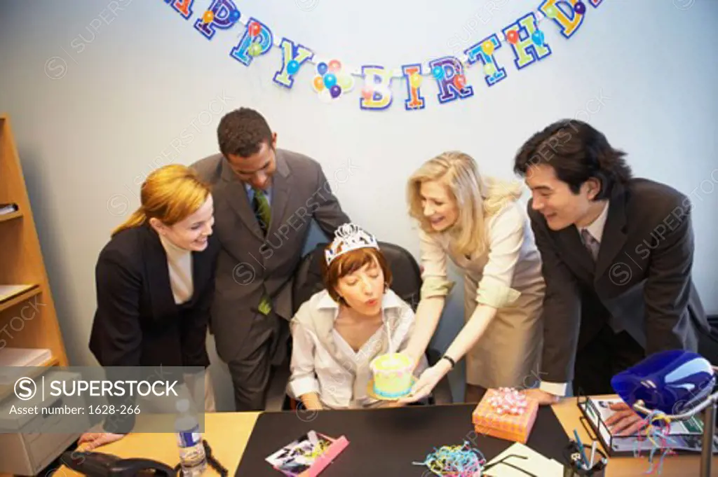 Businesswomen blowing out a candle on her birthday cake with her colleagues standing beside her