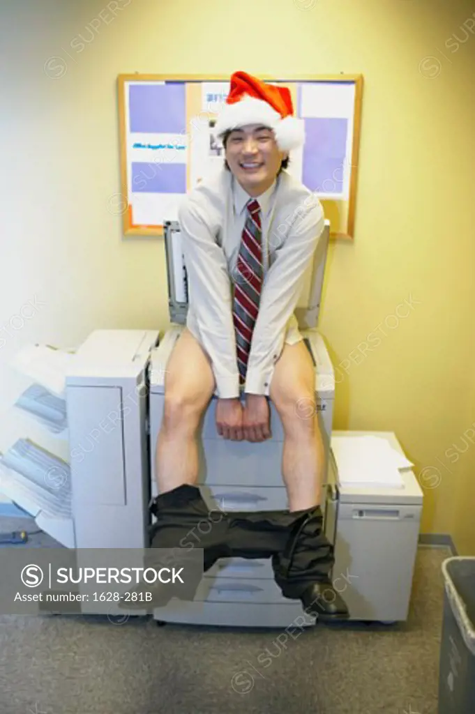 Portrait of a businessman with his pants down sitting on a photocopier wearing a Santa hat